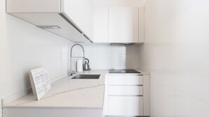 A modern kitchen with white cabinetry, a stainless steel sink, and a kettle. - Il Borgo apartments - A3 (Finale Ligure)