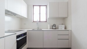 Eine moderne Küche mit weißen Schränken, einem Edelstahlherd, einer Spüle und einem Fenster über der Arbeitsfläche.