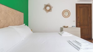 Ein Hotelzimmer mit einem großen Bett, einem hölzernen Kopfteil, einer Wand in Grünton, einer Holztür, einem kleinen Nachttisch und einem an der Wand befestigten Spiegel.
