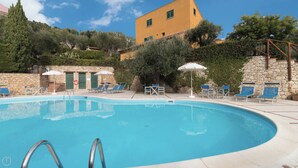 Una piscina con sillas de descanso y sombrillas, rodeada de muros de piedra y follaje.