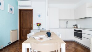 Una cocina moderna con armarios blancos, una mesa de comedor de madera y un jarrón azul con flores.