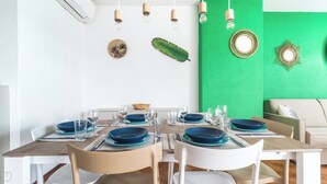 Uma sala de jantar com uma mesa de madeira posta para quatro pessoas, cadeiras brancas e uma parede verde decorativa.