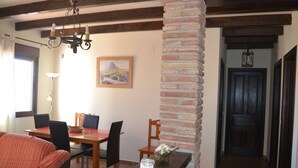 Un espace repas agrémenté d’un pilier en briques, d’une table en bois, de chaises et d’un lustre.