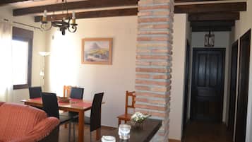 A dining area with a brick column, wooden table, chairs, and a chandelier.
