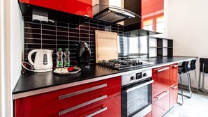 A modern kitchen with red cabinetry, a black countertop, and stainless steel appliances. - Powisle Superior Apartment (Warsaw)