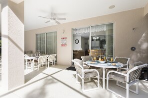 Un patio luminoso con tavolo e sedie, una ventola a soffitto e un cartello che indica le regole della piscina.