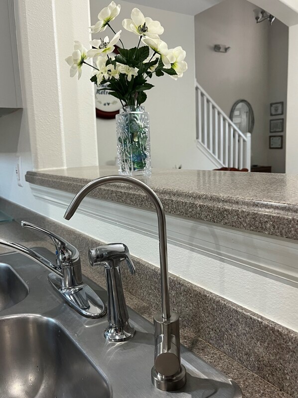 Una cocina con un lavamanos de acero inoxidable, un grifo y un florero con flores blancas sobre la encimera.