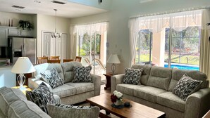 A spacious living room with two grey sofas, a wooden coffee table, and a dining area with a table and chairs. - All 5 star reviews, 6 bed, 5.5 bath, 4 king en-suites, Free pool, spa heat! (Kissimmee)