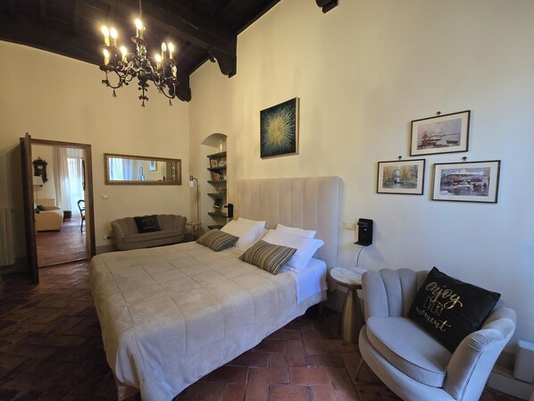 A bedroom with a large bed, a bedside table, a chair, a mirror, and artwork on the walls. - Finestra Dell'Angelo (Pienza)