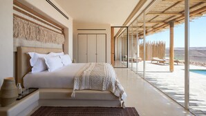 A modern bedroom with a large bed, a view of a pool, and a wooden ceiling structure.