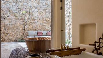 A bathroom with a freestanding bathtub, a stone wall, and a view of the outdoors.