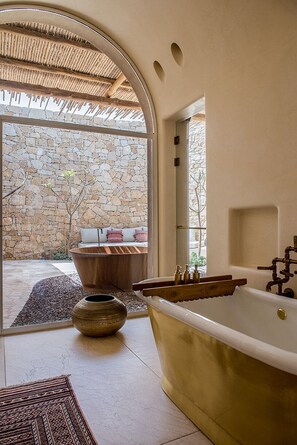 A bathroom with a freestanding bathtub, a stone wall, and a view of the outdoors. - Six Senses Shaharut (Hevel Eilot)