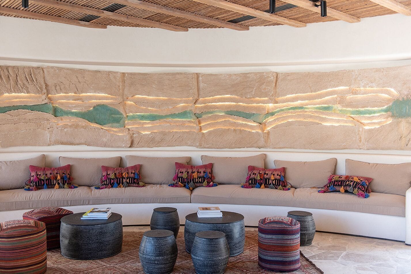 A modern living room with a curved sofa, colorful cushions, and a textured wall art piece.