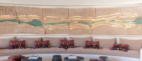 A modern living room with a curved sofa, colorful cushions, and a textured wall art piece.