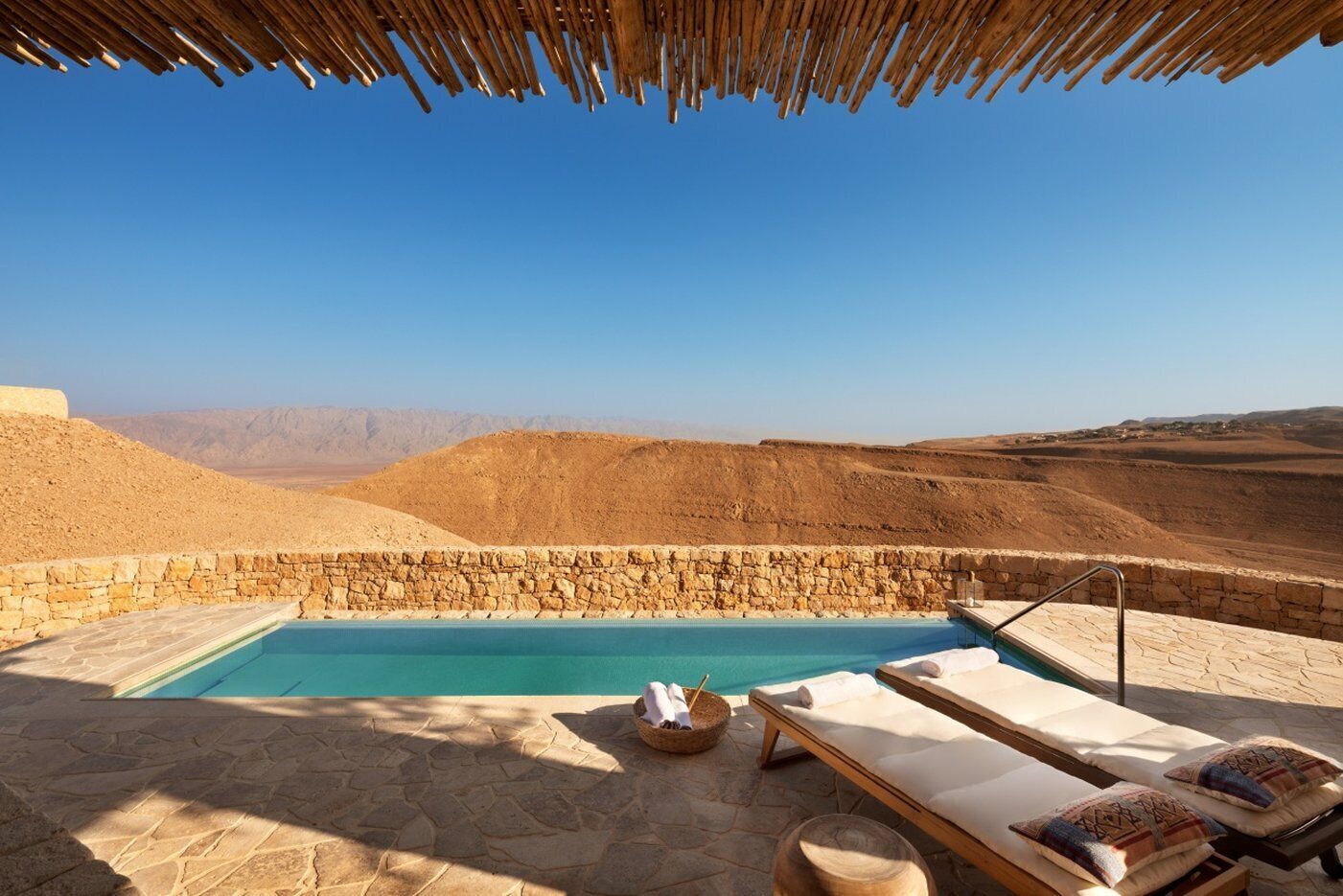A pool area with lounge chairs and a stone wall, overlooking a desert landscape.
