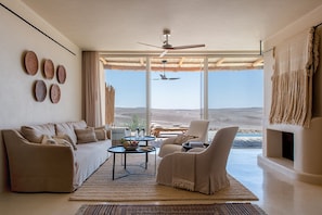 A spacious living room with a large window, a ceiling fan, and a view of the desert landscape. - Six Senses Shaharut (Hevel Eilot)