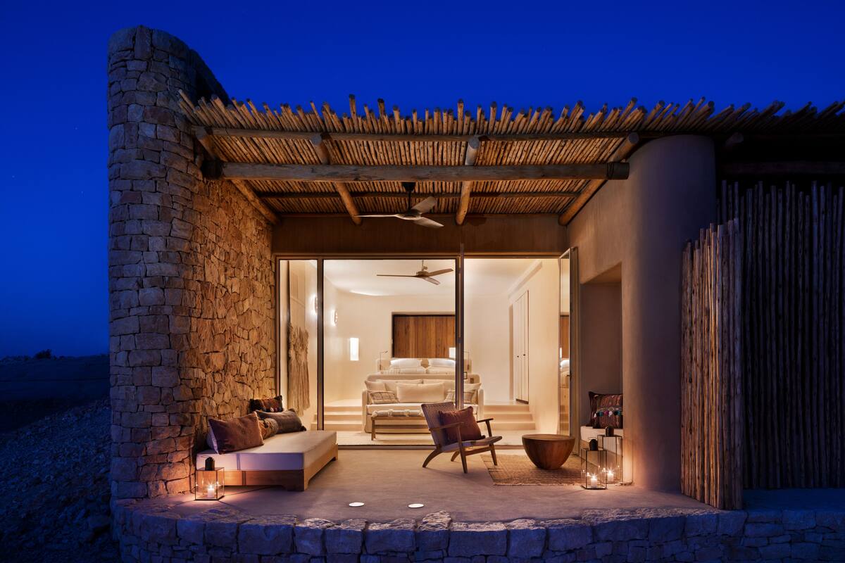 A stone exterior with a covered patio, a bed, and a seating area with a view of the interior.