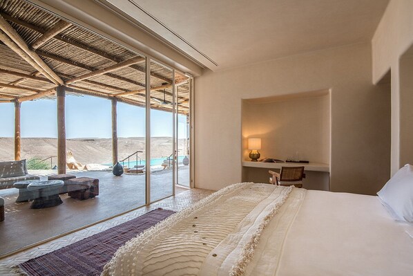 Habitación de hotel con una cama grande, un escritorio con lámpara y vistas a la playa.