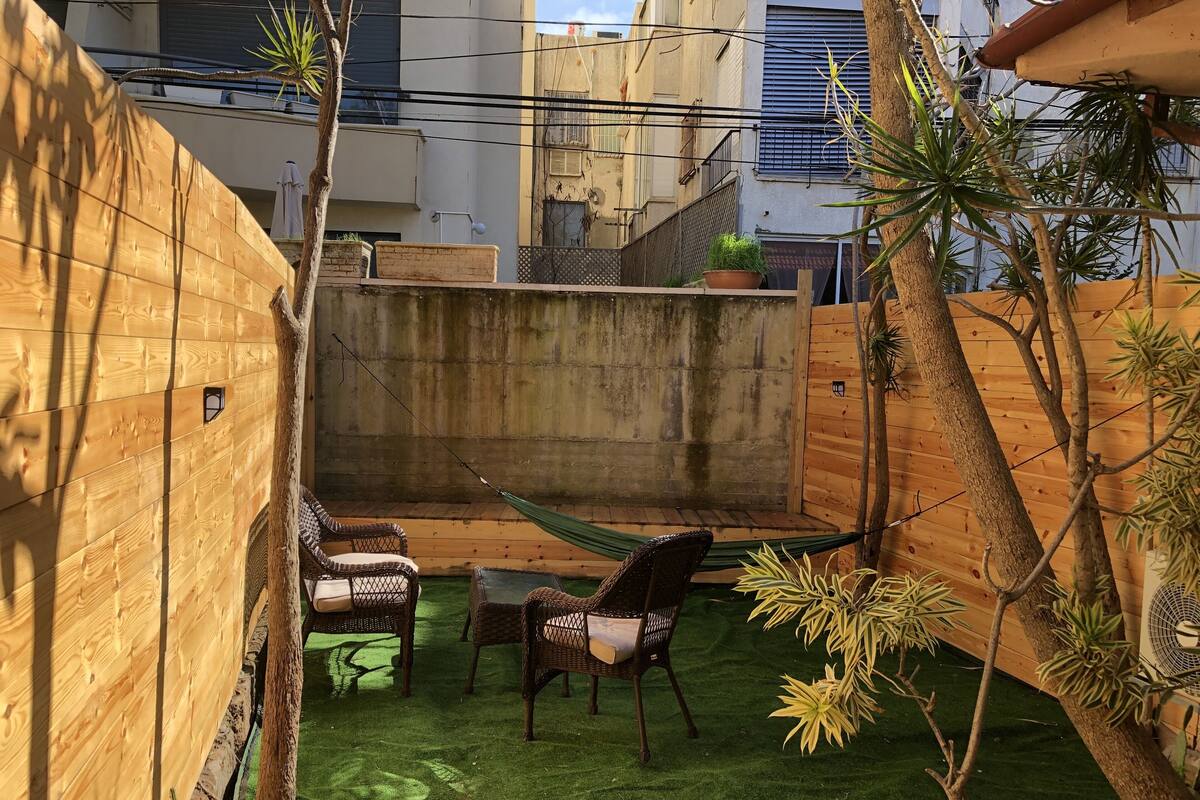 A wooden deck with a hammock, two wicker chairs, and a small table.