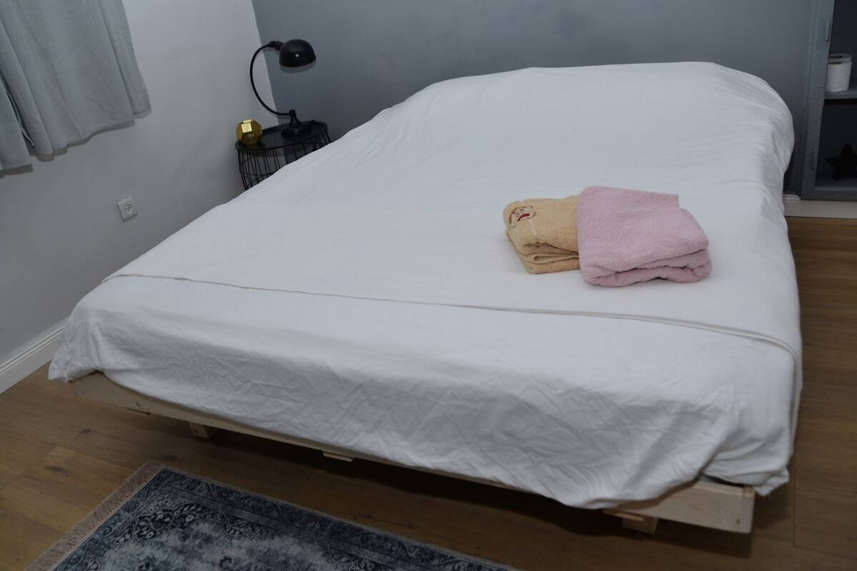 A neatly made bed with a white bedspread, a beige towel, and a pink towel on the side.