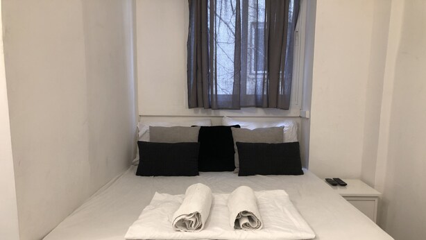 Una cama bien hecha con toallas enrolladas, una mesita de noche con un control remoto y una ventana con cortinas.