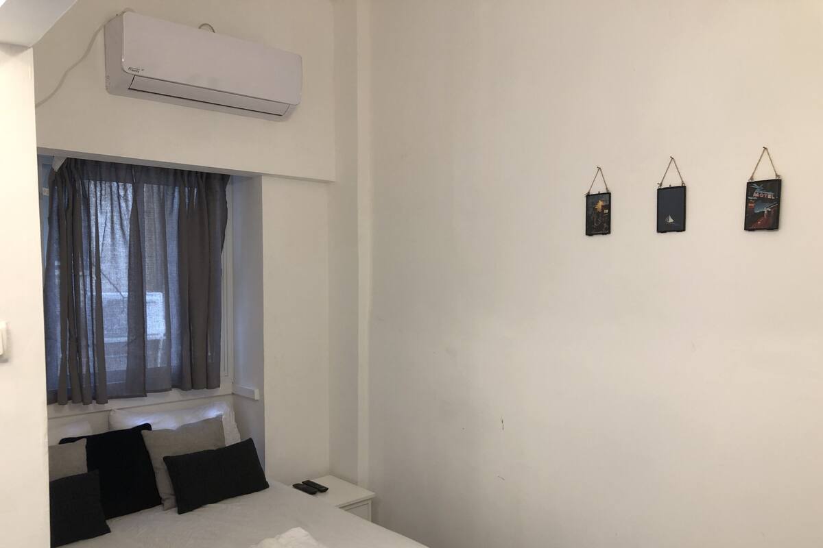 Ein Hotelzimmer mit einem Bett, einem Nachttisch, einem Fenster mit Vorhängen, einer Klimaanlage und drei Wanddekorationen.