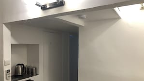 A narrow hallway with a white door on the left, a black refrigerator, and a shelf with kitchen items. - Arnon-6 - Adults Only (Tel Aviv)