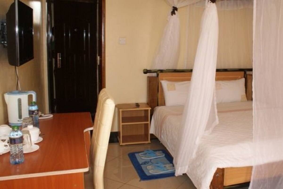 Un dormitorio con una cama cubierta por un dosel, una mesita de noche de madera, una mesa con tazas y botellas, y una silla.