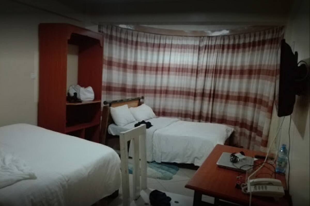 Habitación de hotel con dos camas, un escritorio con un teléfono y una botella, y un armario rojo.