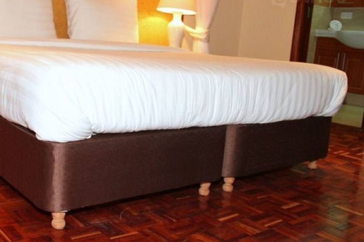 Una cama grande con estructura de madera y ropa de cama blanca en una habitación con suelo de madera en patrón de espiga.