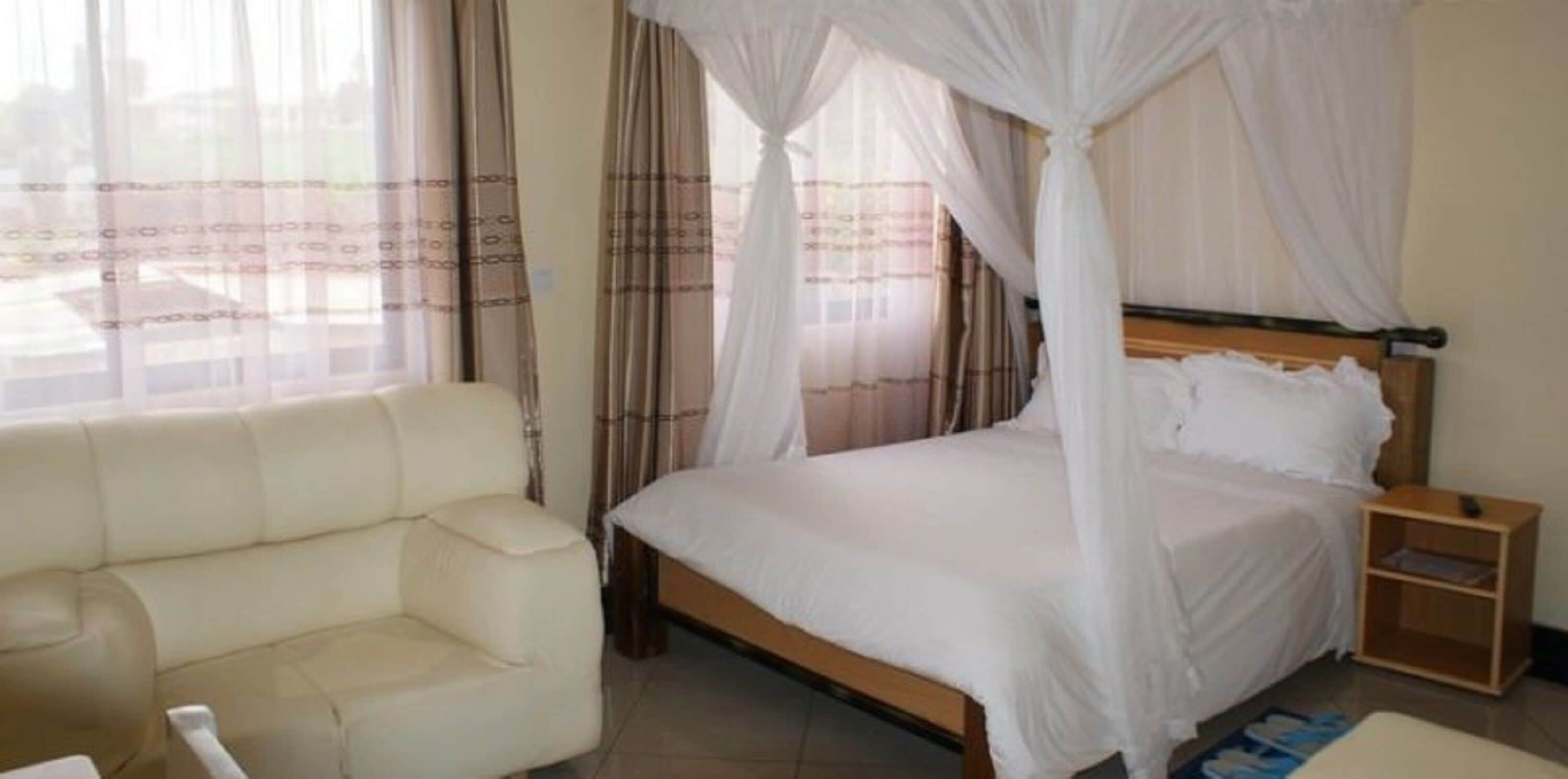 A room with a bed covered by a canopy, a sofa, and a nightstand.
