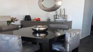Een eetgedeelte met een zwarte tafel, vier grijze fauteuils, een ronde spiegel en een set kaarsen op een grijze console tafel.