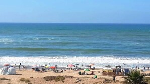 Een strand met parasols, mensen, een zandstrand en de oceaan.