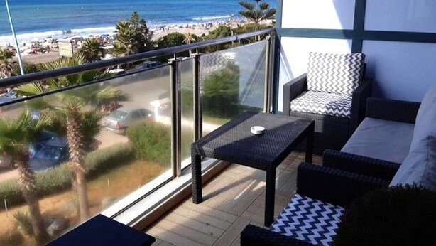 Een balkon met uitzicht op het strand en de oceaan, voorzien van een stoel en een klein tafeltje.