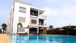 A modern building with a swimming pool, balconies, and outdoor seating. - Residence Galets Sur Mer 4701 (Dar Bouazza)