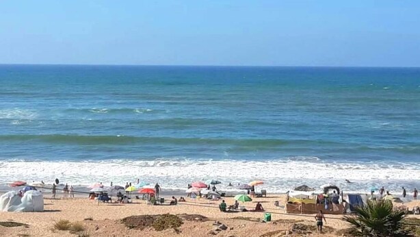 Ein Strand mit Sonnenschirmen und Menschen, ein sandiger Uferstreifen und das Meer.