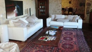 Un salon avec deux canapés blancs, une table basse avec des magazines, un tapis et une bibliothèque.