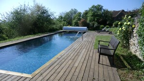 Une terrasse en bois avec une piscine, un banc et un espace abrité équipé de chaises longues.