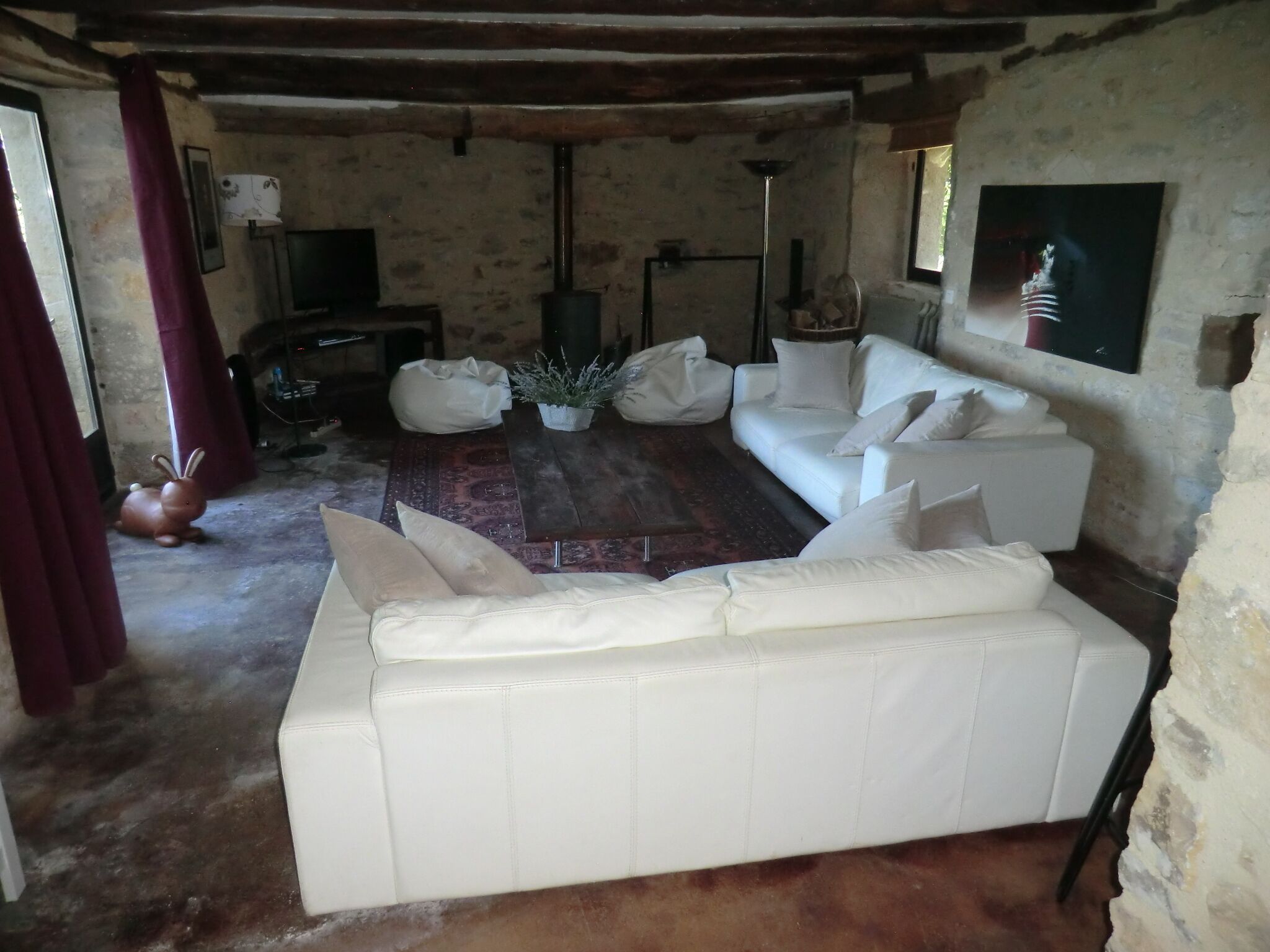 A rustic living room with a white leather sofa, a patterned rug, and a stone wall.