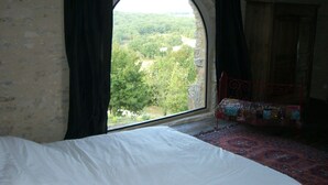 Une chambre dotée d’une grande fenêtre en arc d’où l’on peut admirer un paysage boisé.