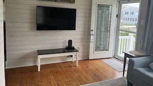 Ein Wohnzimmer mit einem flachbildfernseher an einer weißen Wand, einer Bank und einer Glastür zum Balkon.
