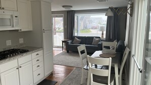 Eine moderne Küche mit weißen Schränken, einer Mikrowelle und einem Herd. Es gibt einen Essbereich mit Tisch und Stühlen, und ein graues Sofa im Hintergrund.