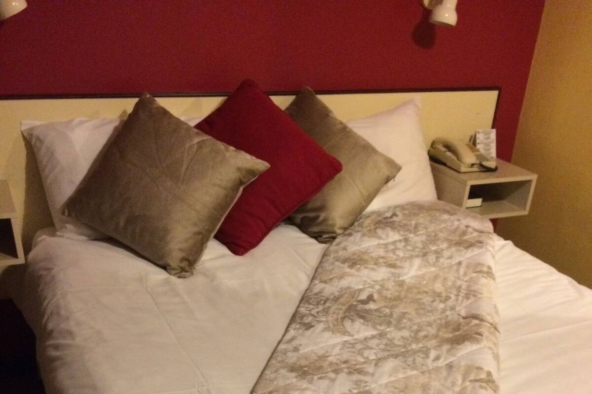Una cama con colcha estampada, almohadas y una mesita de noche con lámpara y teléfono.