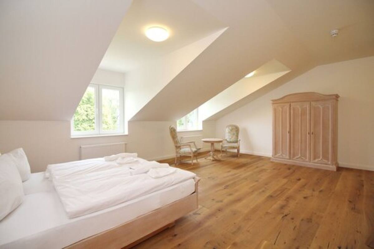 A bedroom with a large bed, a wooden floor, a wardrobe, and a small table with chairs.