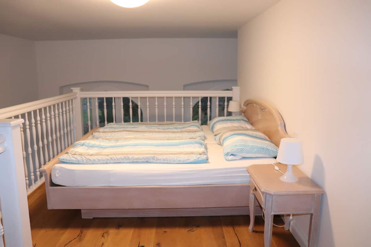 A bedroom with a wooden bed, white walls, and a small bedside table with a lamp.