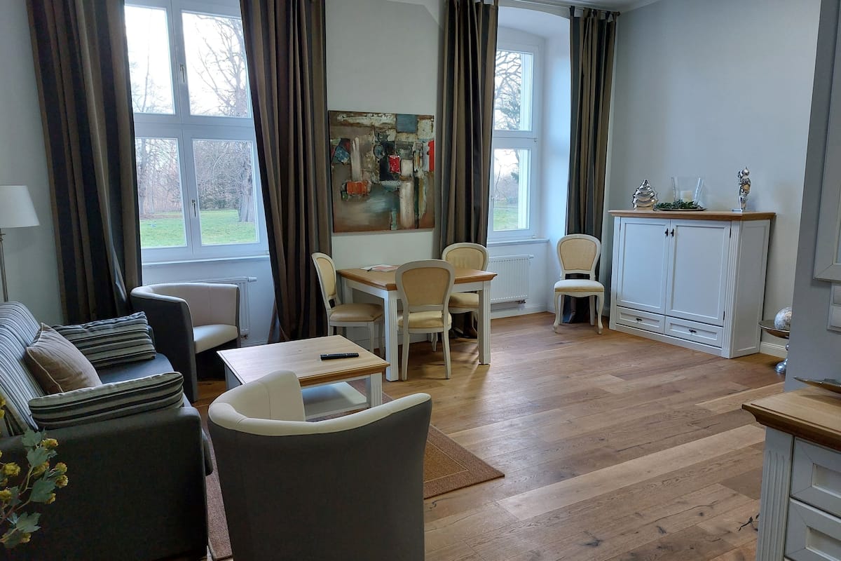 A modern living room with a sofa, a dining table with chairs, a cabinet, and a large window with curtains.
