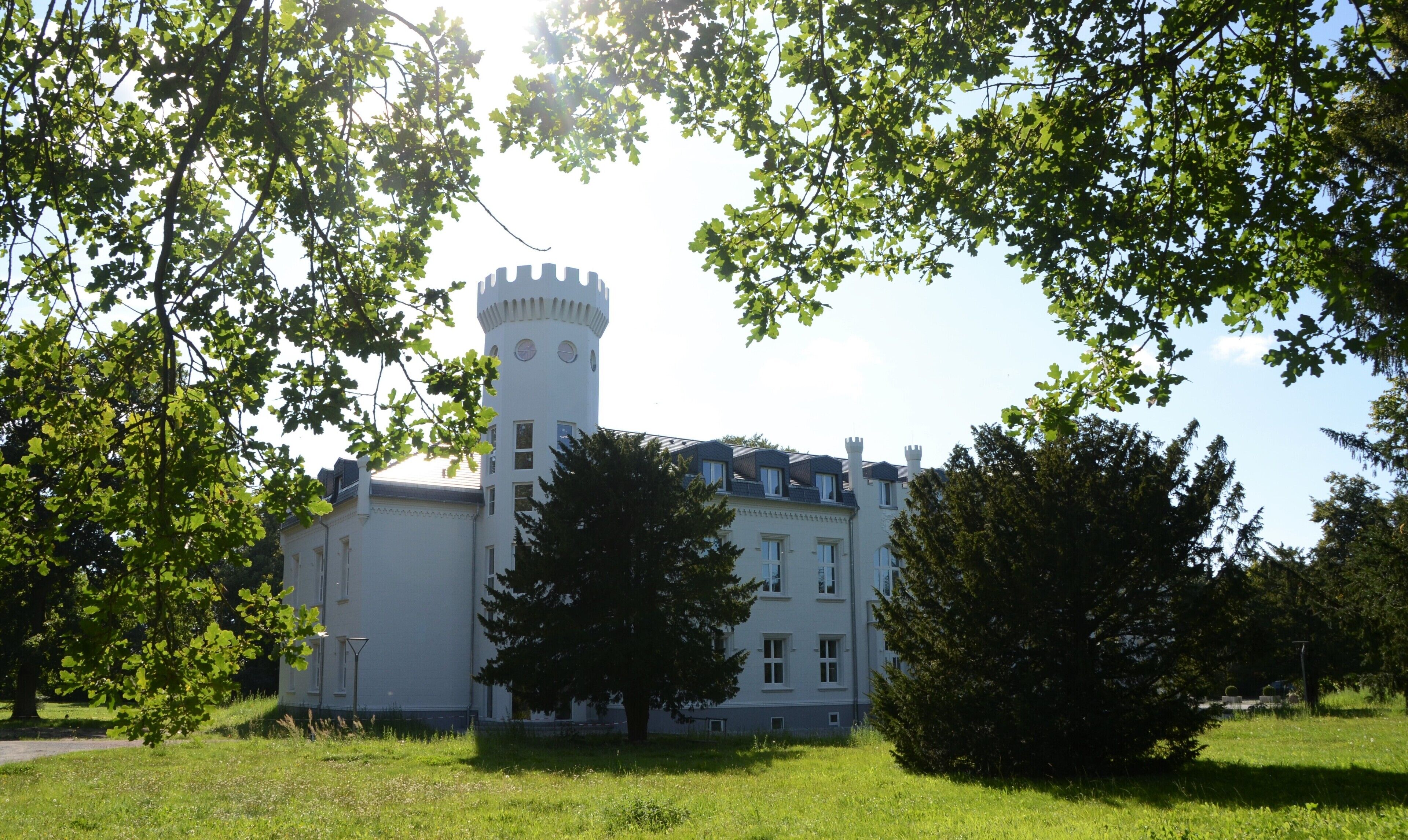 Un edificio al estilo de castillo con una torre, rodeado de árboles y césped.