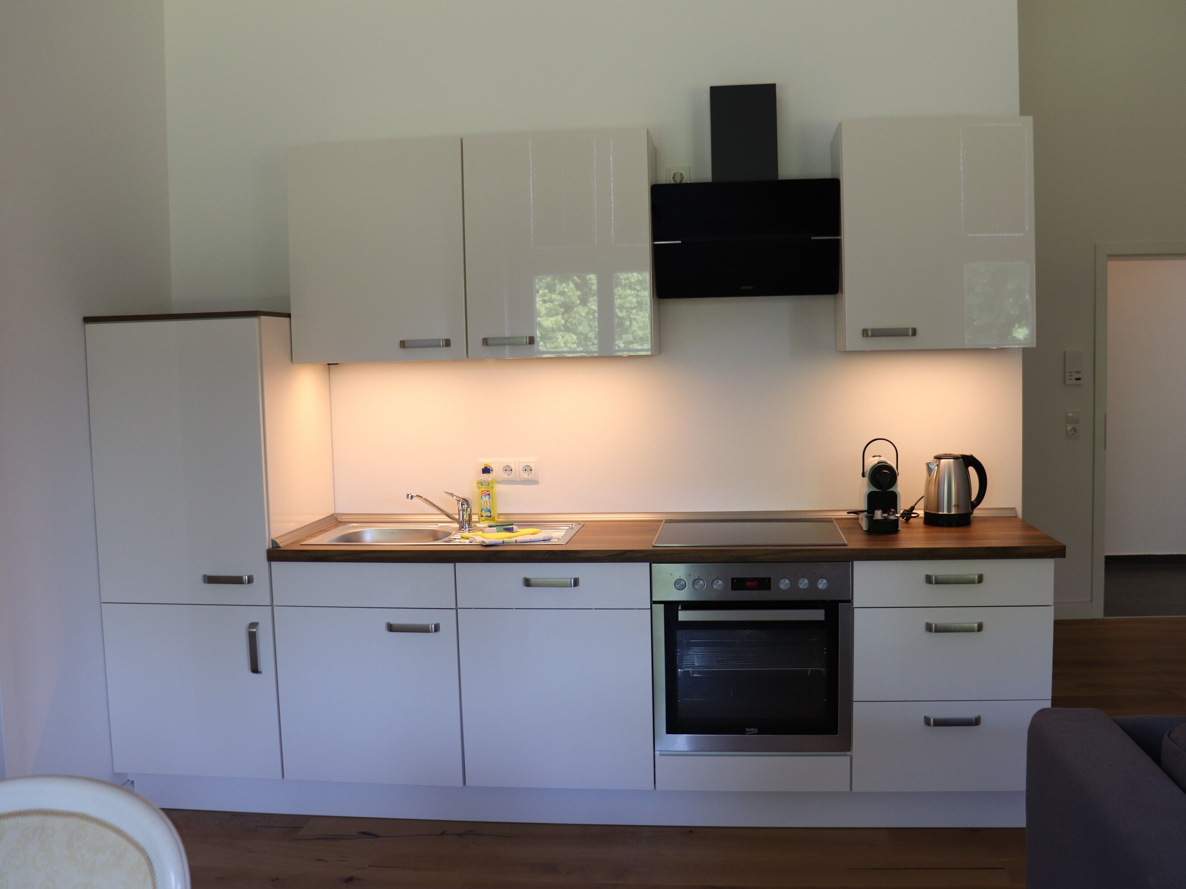 Una cocina moderna con gabinetes blancos, horno empotrado y cafetera.
