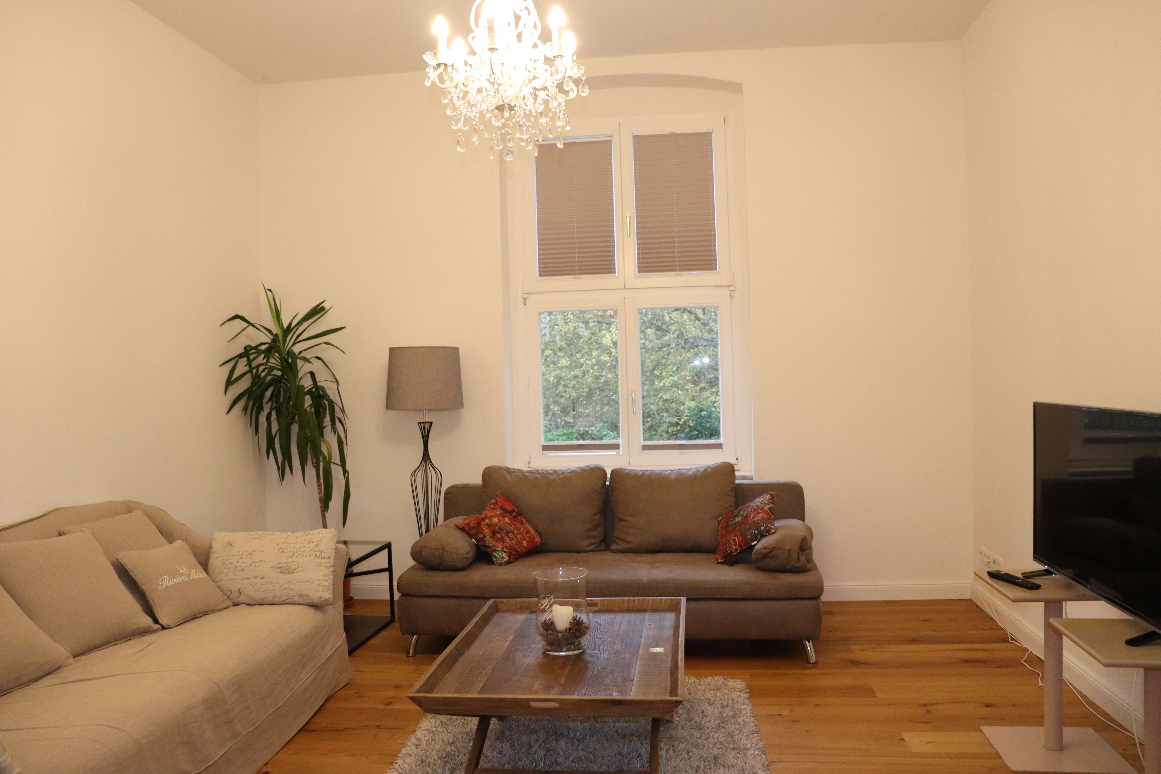 Ein Wohnzimmer mit einer Couch, einem Couchtisch, einem Fernseher, einer Lampe und einem Fenster mit Jalousien.
