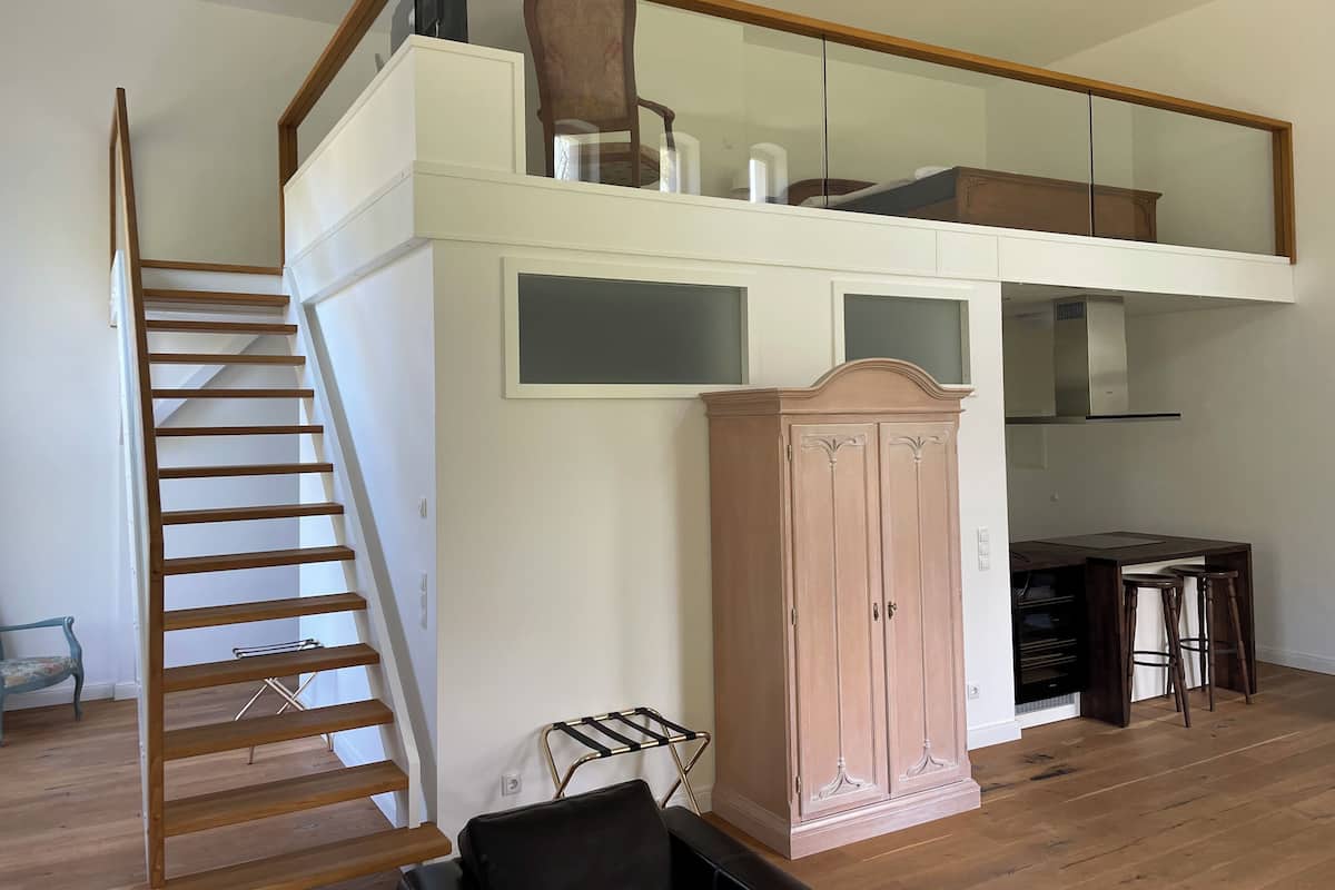 A spacious loft with a wooden staircase, a large wardrobe, and a dining area with stools.